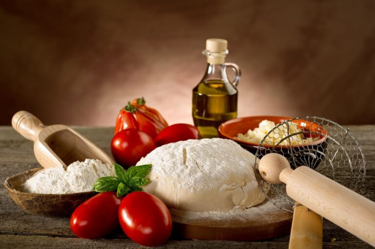 Pizza dough and other pizza ingredients on table.
