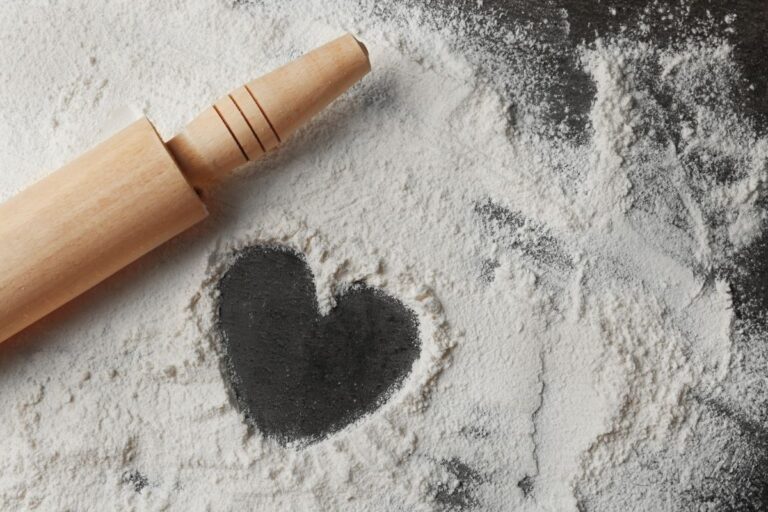 Top view shot of flour with a heart formation and a rolling on a grey background.